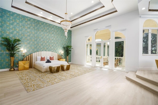 bedroom featuring multiple windows, light wood-type flooring, french doors, and a raised ceiling