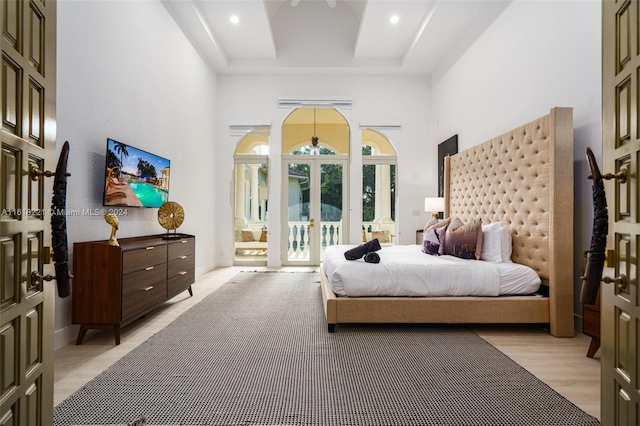 bedroom featuring a high ceiling, french doors, a raised ceiling, light hardwood / wood-style floors, and access to exterior