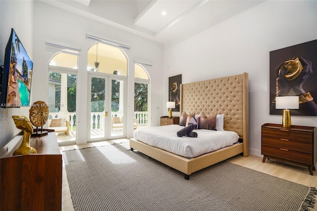 bedroom with light wood-type flooring, access to exterior, french doors, and a towering ceiling