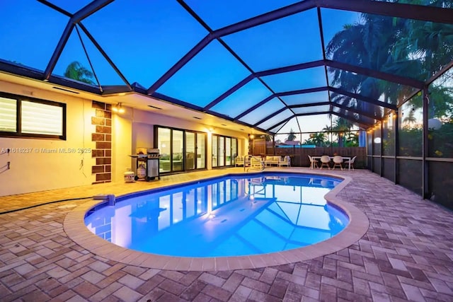 pool at dusk featuring area for grilling, a lanai, and a patio area