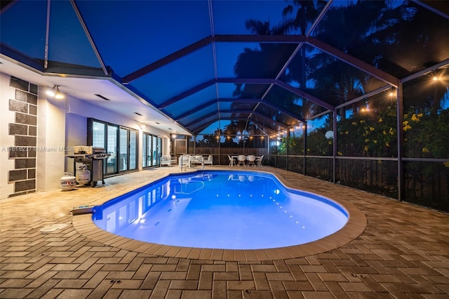 pool at night featuring a lanai and a patio