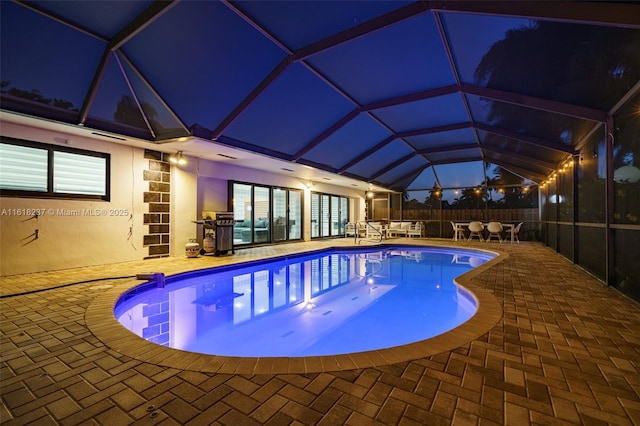 pool at twilight with a patio area and glass enclosure