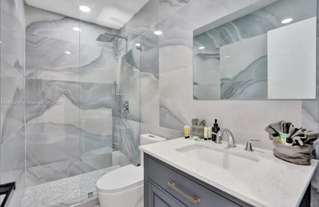 bathroom featuring tiled shower, vanity, toilet, and tile walls