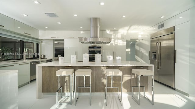 kitchen with a spacious island, a breakfast bar area, white cabinetry, island range hood, and stainless steel appliances