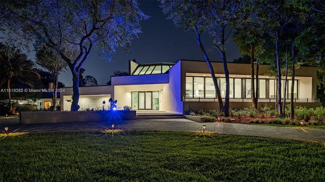 back house at night featuring a lawn