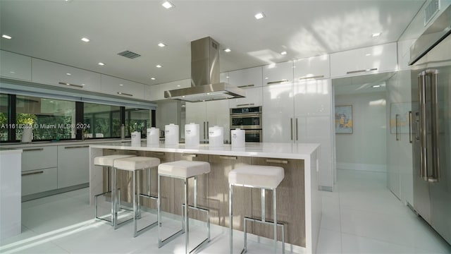 kitchen featuring double oven, a kitchen bar, island exhaust hood, light tile patterned floors, and a spacious island