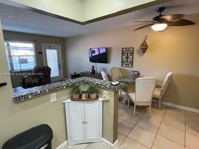 kitchen with light tile patterned floors, a textured ceiling, tile counters, and ceiling fan