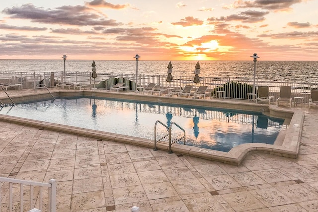 pool at dusk featuring a patio area and a water view