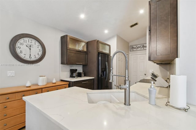 kitchen with stainless steel fridge, vaulted ceiling, sink, and light stone counters