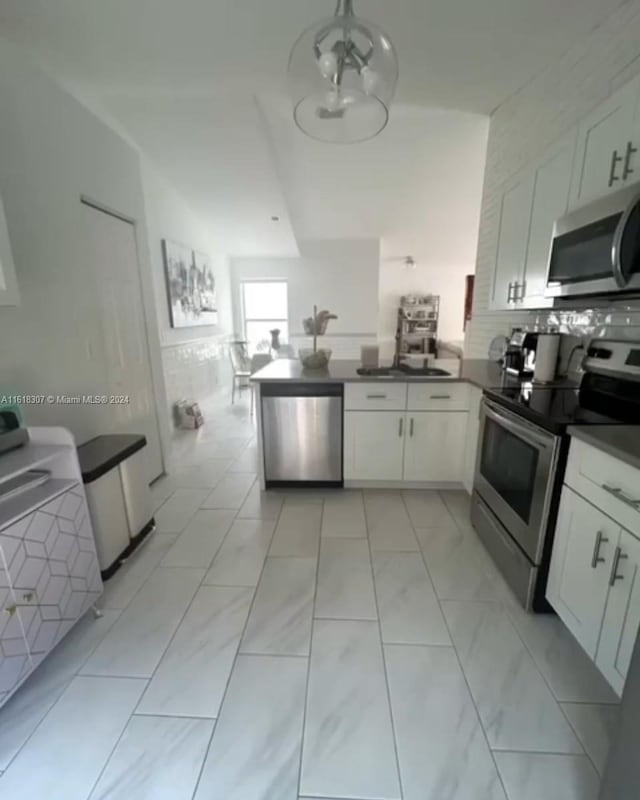 kitchen with light tile patterned flooring, white cabinetry, kitchen peninsula, and stainless steel appliances