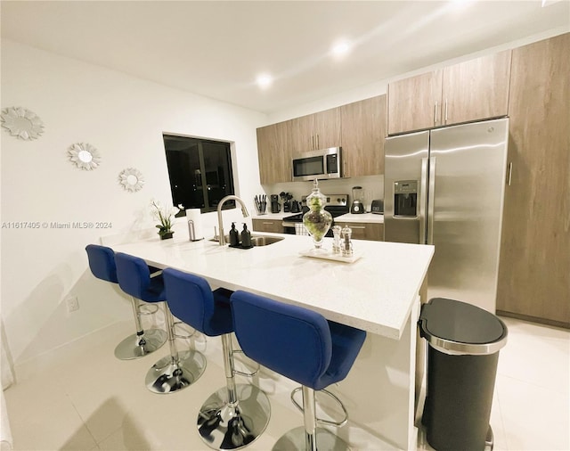 kitchen featuring light tile patterned floors, appliances with stainless steel finishes, sink, and a kitchen bar