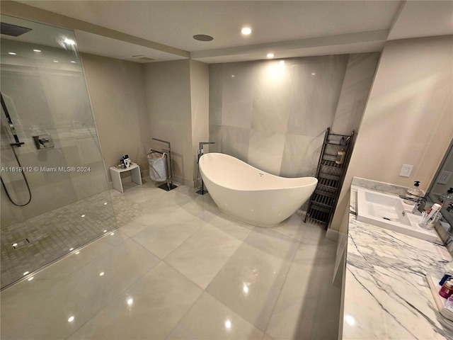 bathroom with tile walls, independent shower and bath, tile patterned floors, and vanity