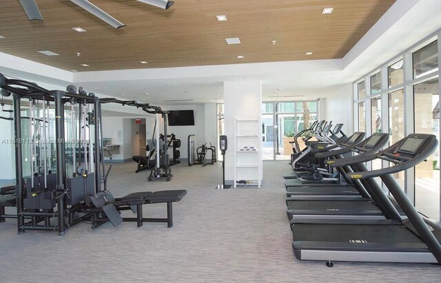 exercise room with a tray ceiling, carpet floors, and wooden ceiling