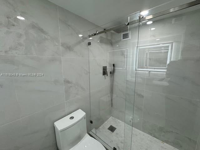 bathroom featuring walk in shower, tile walls, and toilet