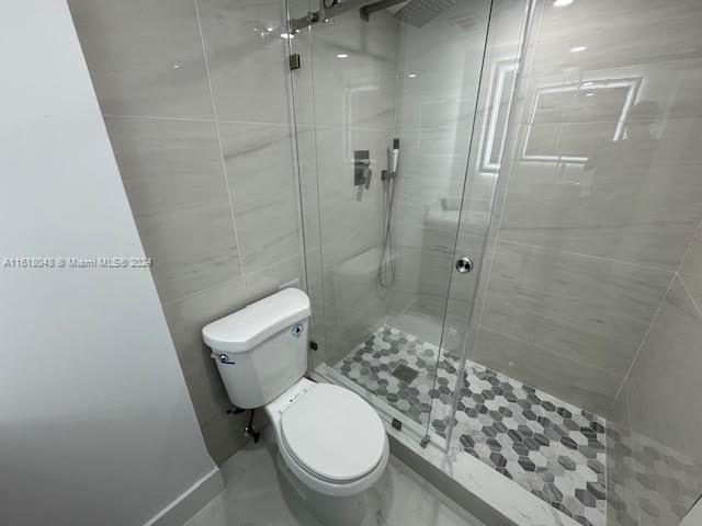 bathroom featuring toilet, an enclosed shower, and tile walls