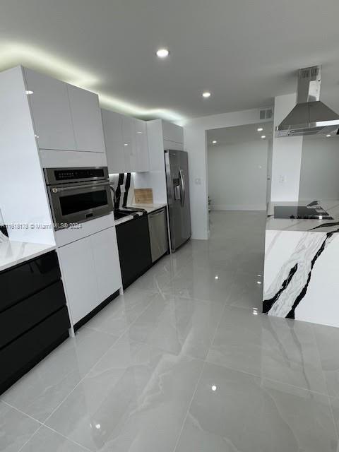 kitchen with white cabinetry, stainless steel appliances, light tile patterned floors, and wall chimney range hood