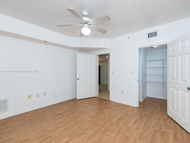 unfurnished bedroom with ceiling fan, a walk in closet, a closet, and light hardwood / wood-style floors