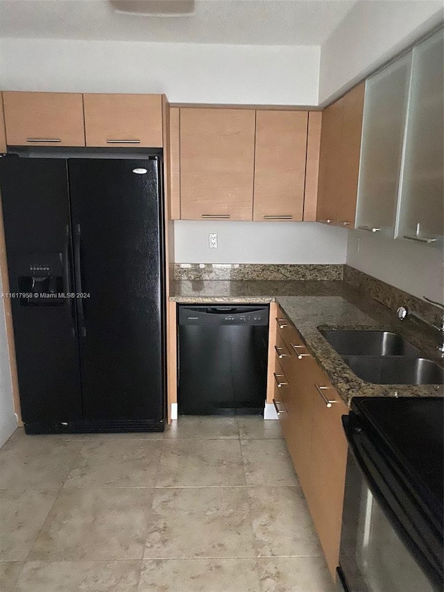 kitchen with dark stone counters, black appliances, light tile patterned floors, and sink