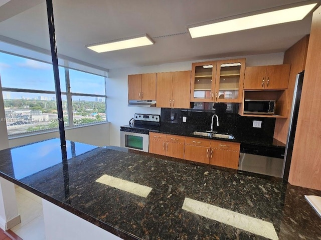 kitchen with sink, dark stone counters, stainless steel appliances, kitchen peninsula, and decorative backsplash