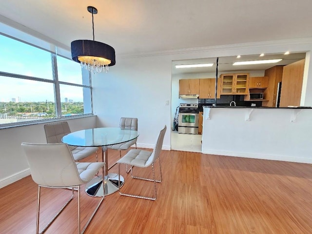 dining area with sink, light wood-type flooring, crown molding, and an inviting chandelier