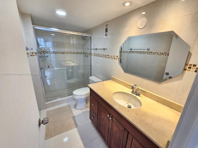 bathroom featuring tile patterned floors, toilet, tile walls, vanity, and walk in shower