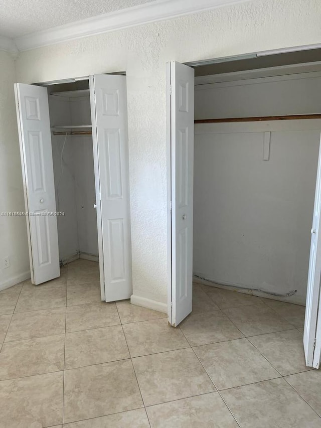 unfurnished bedroom featuring light tile patterned flooring, a textured ceiling, a closet, and ornamental molding