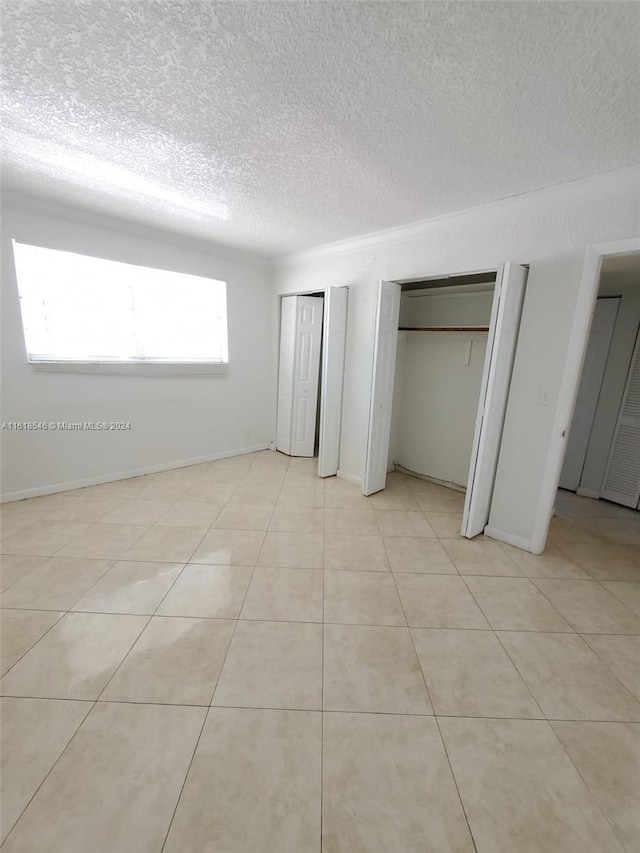 unfurnished bedroom with multiple closets, a textured ceiling, and light tile patterned floors