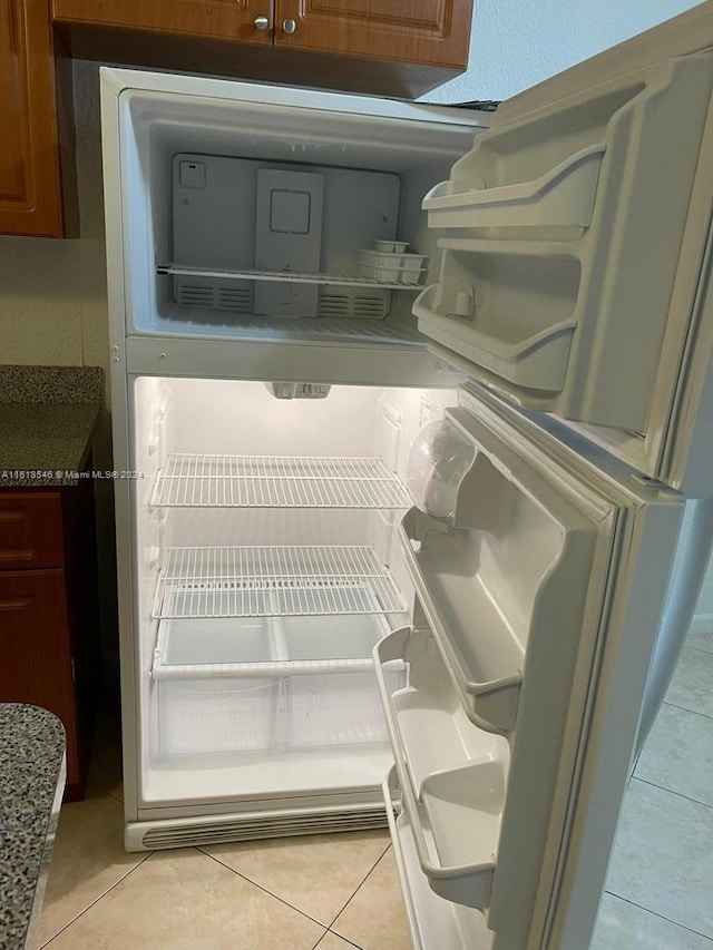 room details with light tile patterned flooring, light stone countertops, and refrigerator