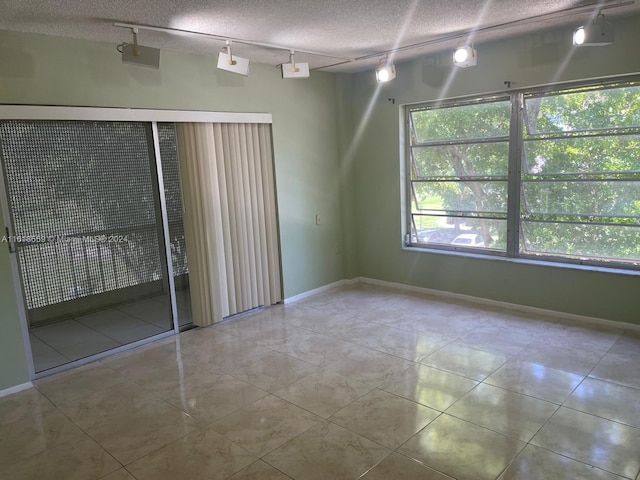 spare room featuring track lighting, a textured ceiling, a wealth of natural light, and light tile patterned floors