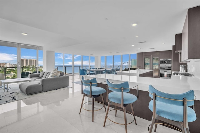 interior space with a breakfast bar area, dark brown cabinets, light tile patterned floors, a water view, and appliances with stainless steel finishes