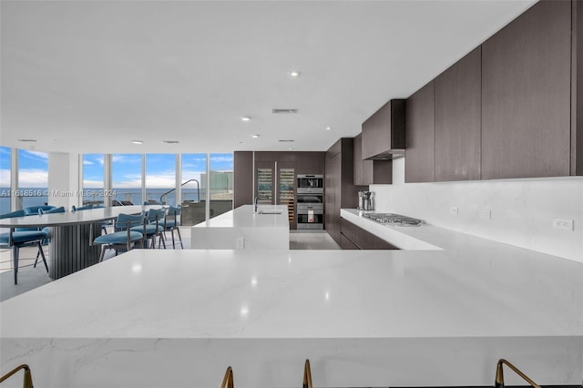 kitchen featuring sink, stainless steel gas cooktop, a water view, a center island, and light stone countertops