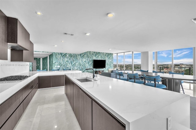 kitchen with stainless steel gas stovetop, sink, expansive windows, dark brown cabinets, and a spacious island