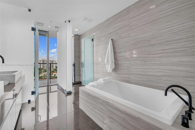 bathroom with independent shower and bath, vanity, and tile walls