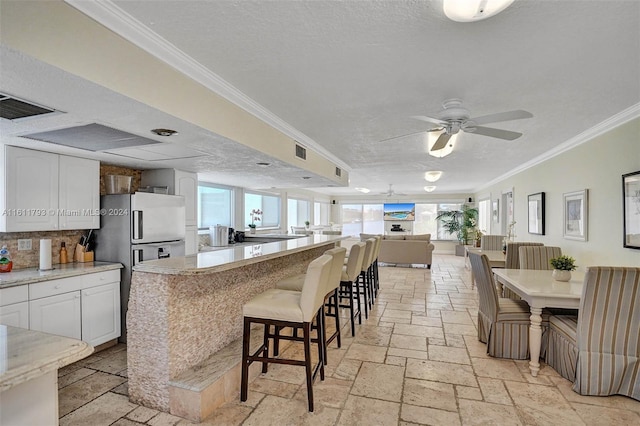 kitchen with a kitchen bar, crown molding, white cabinets, and a healthy amount of sunlight