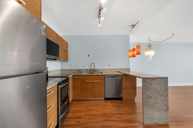 kitchen featuring rail lighting, hardwood / wood-style floors, sink, appliances with stainless steel finishes, and kitchen peninsula