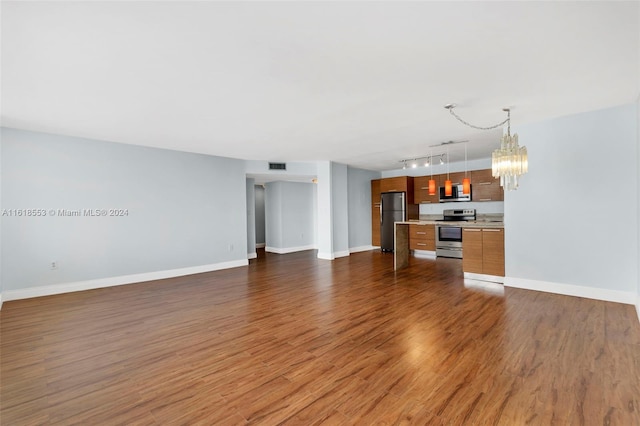 unfurnished living room featuring an inviting chandelier, dark wood-type flooring, and track lighting