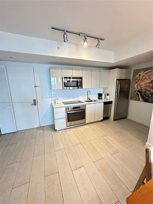 kitchen with sink, white cabinetry, light hardwood / wood-style flooring, stainless steel appliances, and backsplash