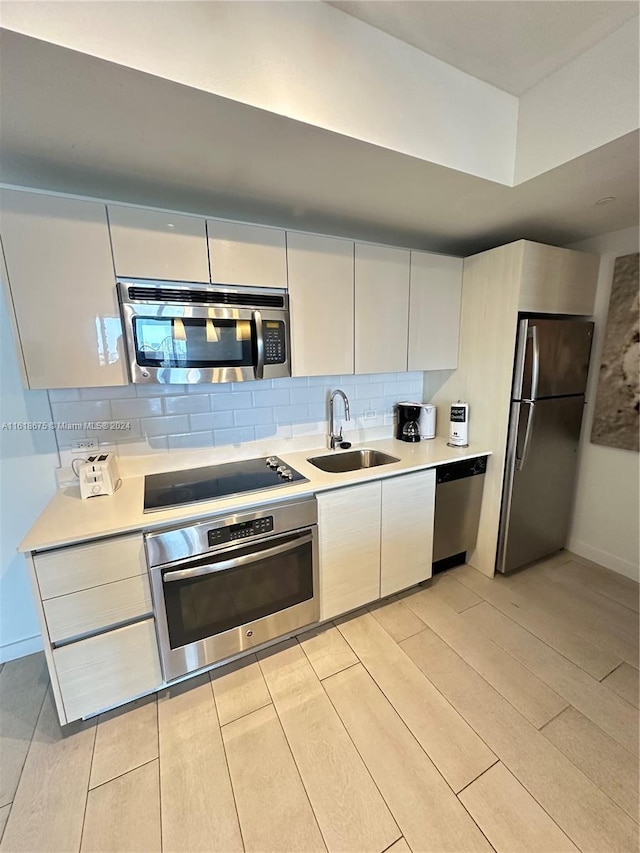 kitchen with sink, light wood-type flooring, appliances with stainless steel finishes, decorative backsplash, and white cabinets