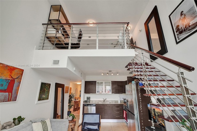 staircase featuring sink, rail lighting, a towering ceiling, and light tile patterned floors