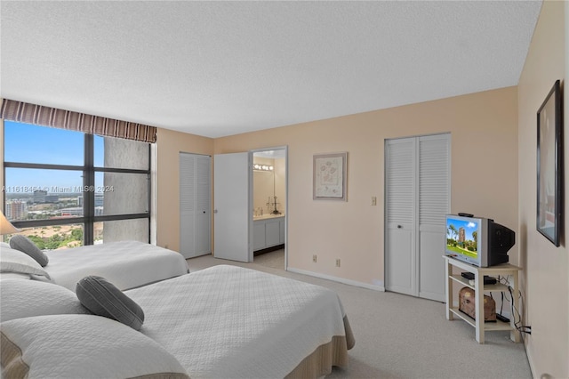 bedroom featuring light carpet, multiple closets, a textured ceiling, and ensuite bath