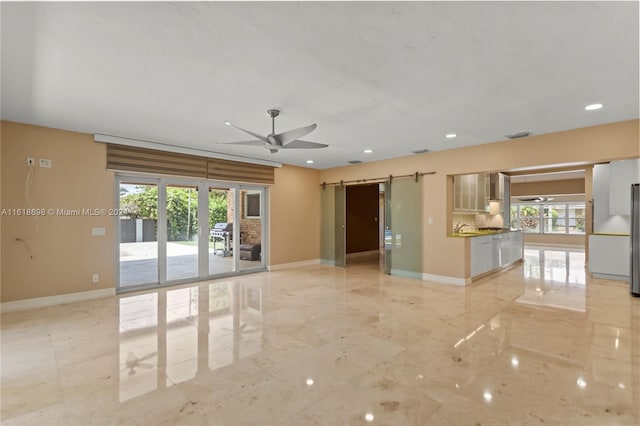 unfurnished room featuring a wealth of natural light, ceiling fan, and a barn door