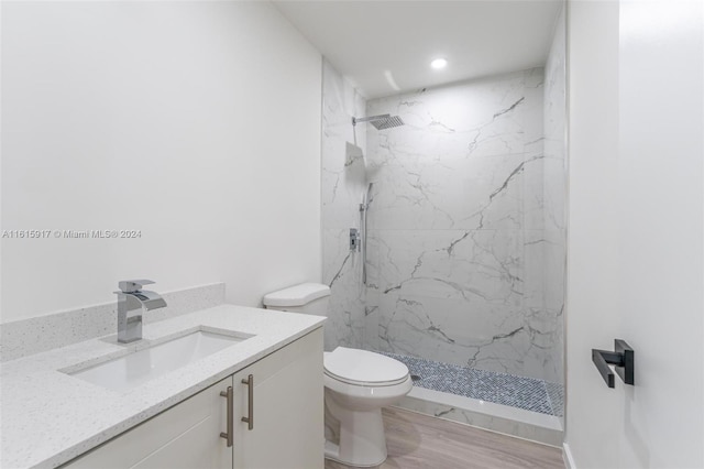 bathroom featuring wood-type flooring, vanity, toilet, and tiled shower