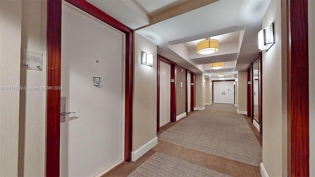 corridor featuring baseboards and a tray ceiling