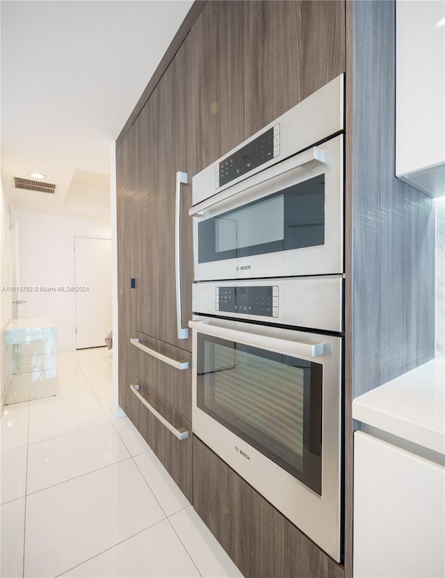 kitchen featuring dark brown cabinetry, double oven, and light tile patterned floors