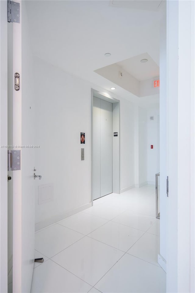 hallway featuring light tile patterned flooring, elevator, and a tray ceiling