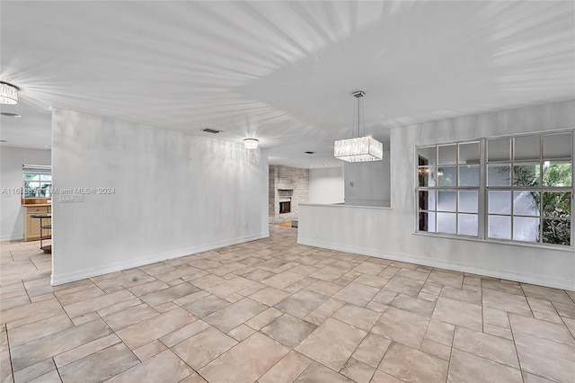 unfurnished room featuring a stone fireplace and an inviting chandelier