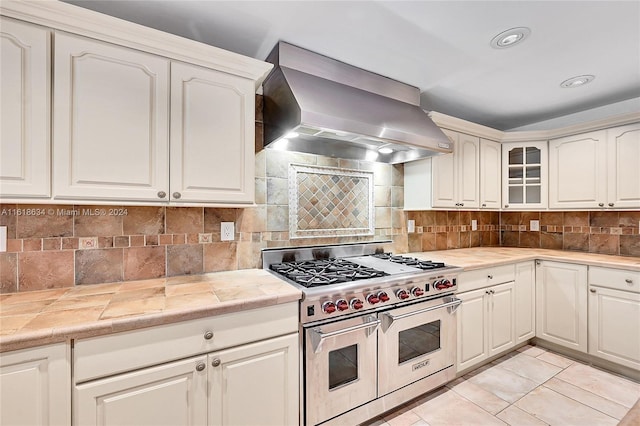 kitchen featuring backsplash, tile counters, wall chimney exhaust hood, and double oven range