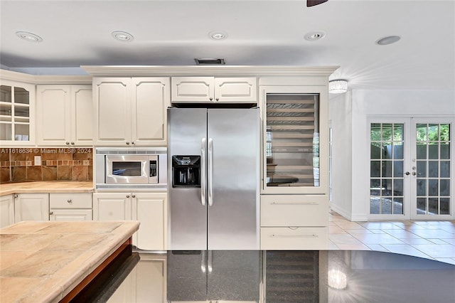 kitchen with french doors, decorative backsplash, appliances with stainless steel finishes, light tile patterned flooring, and white cabinetry