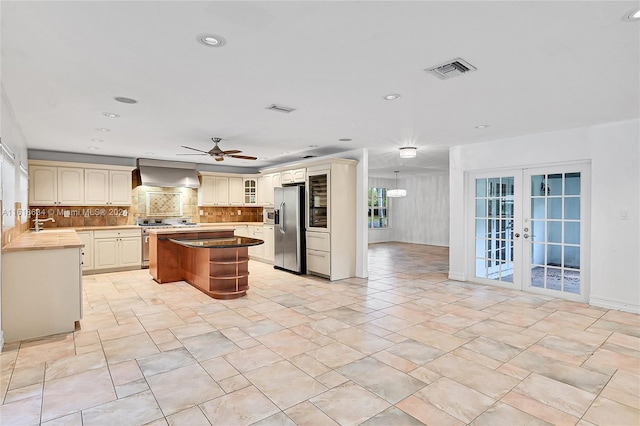 kitchen with french doors, a center island, wall chimney range hood, decorative backsplash, and appliances with stainless steel finishes