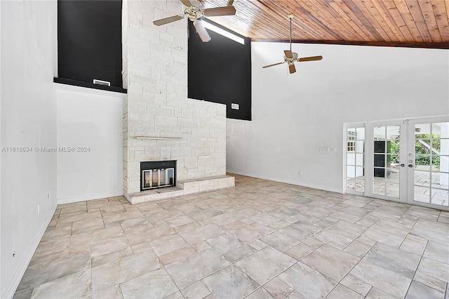 unfurnished living room with french doors, ceiling fan, high vaulted ceiling, wooden ceiling, and a stone fireplace